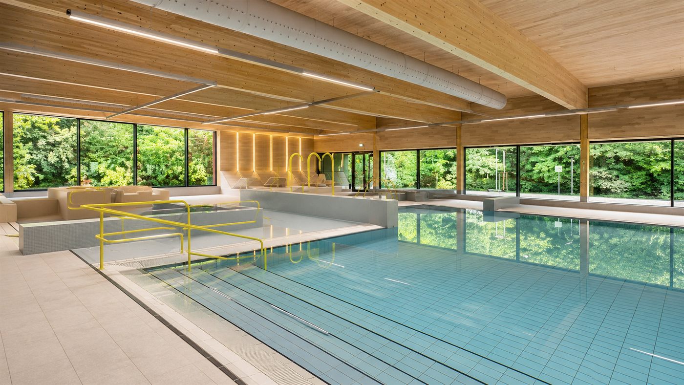 Schwimmhalle mit Holzdecke und bodentiefen Fenstern